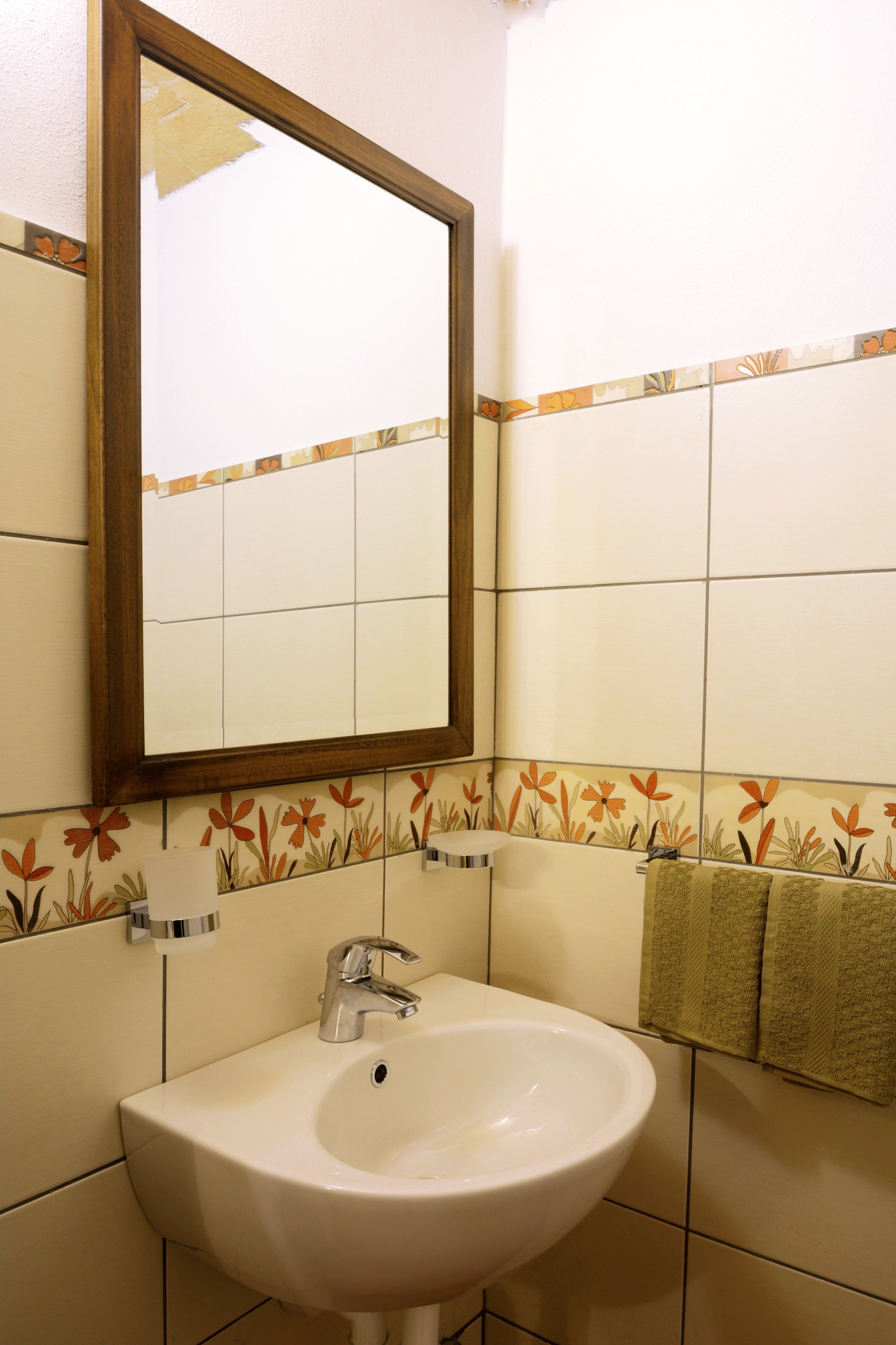 A bathroom with a white sink, a mirror, and floral-patterned tiles.