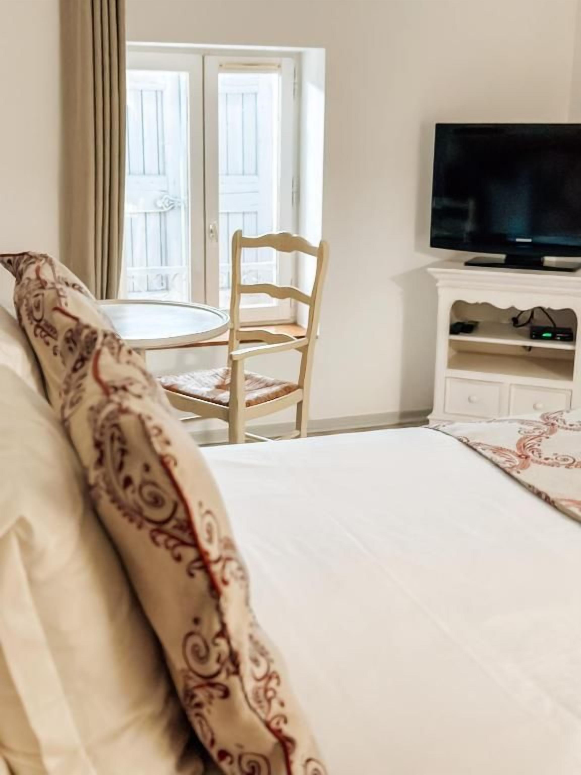 A hotel room with a bed, a television on a stand, a chair, and a small table.