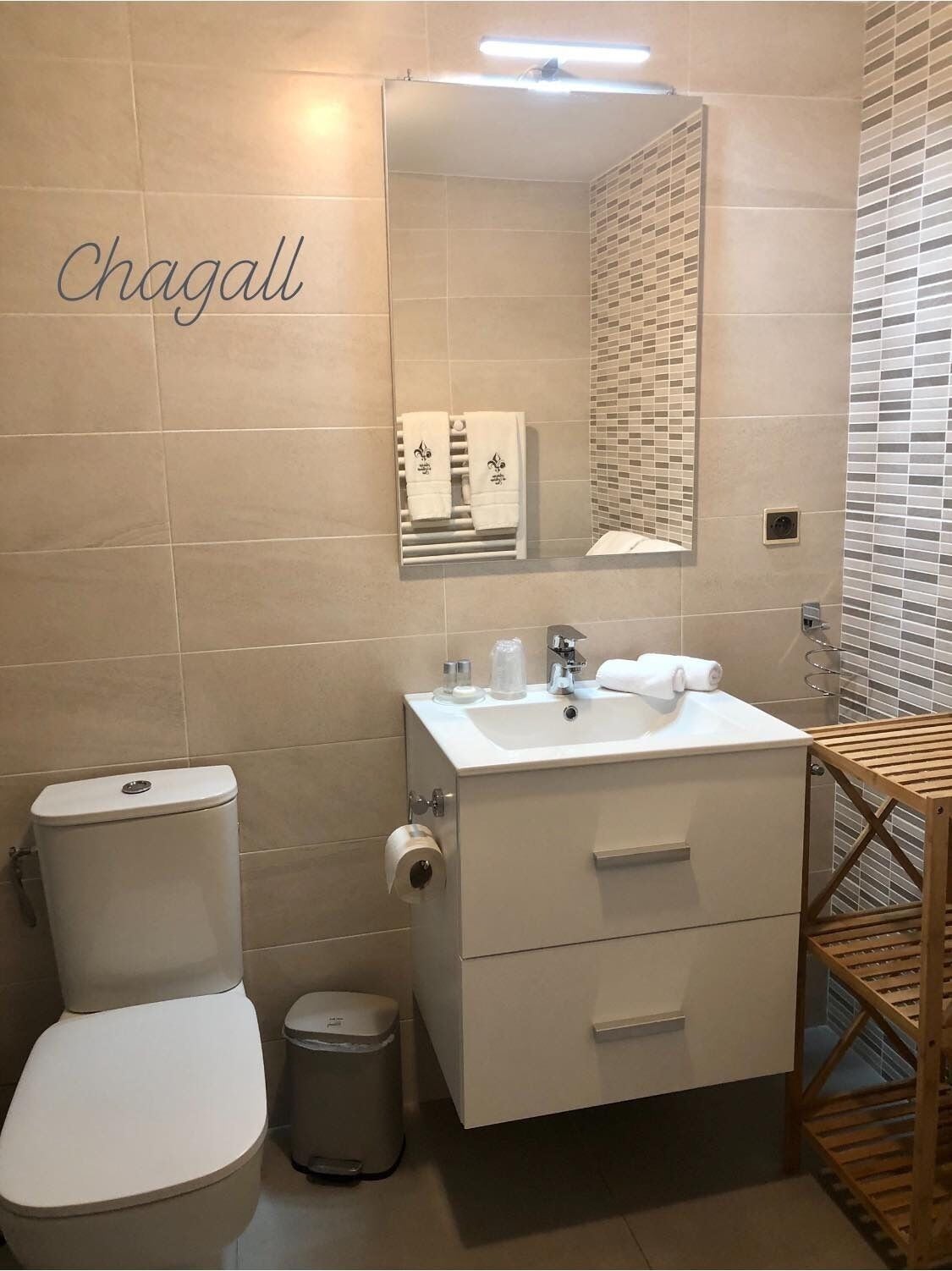 A bathroom with a toilet, sink, mirror, and towel rack.