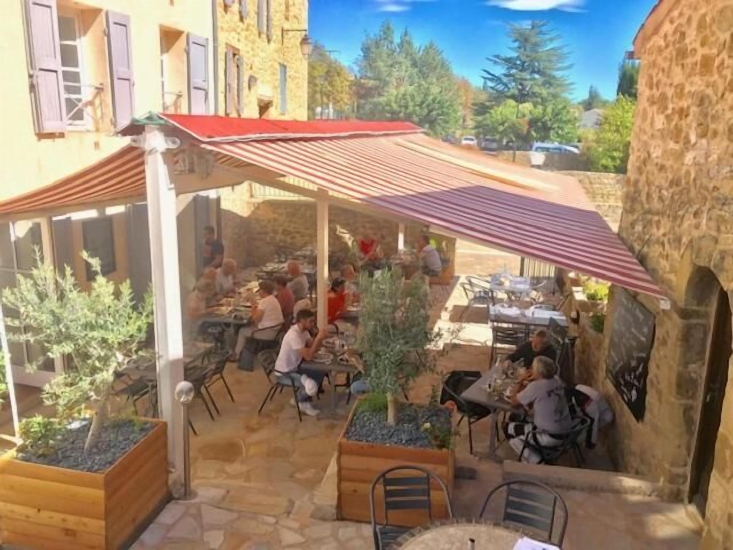 Un café al aire libre con suelo de piedra, macetas de madera y mesas y sillas de metal.