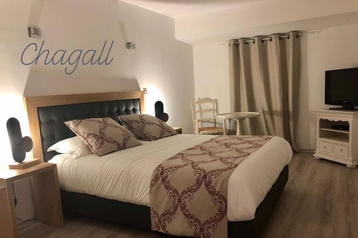 Quarto bem arrumado com cama, mesa de cabeceira, cadeira e televisão.