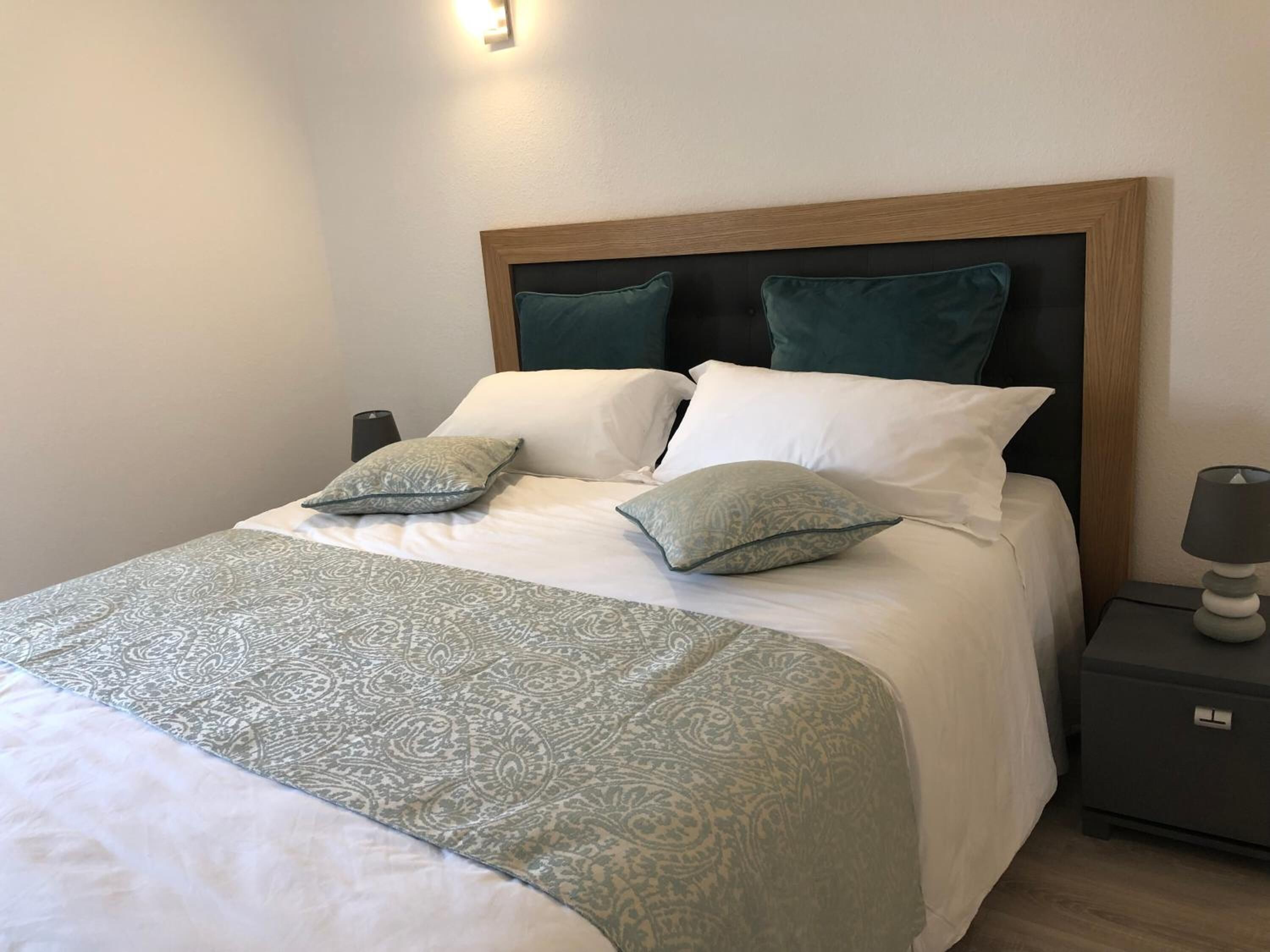 A neatly made bed with a patterned bedspread, two pillows, and a bedside table with a lamp.