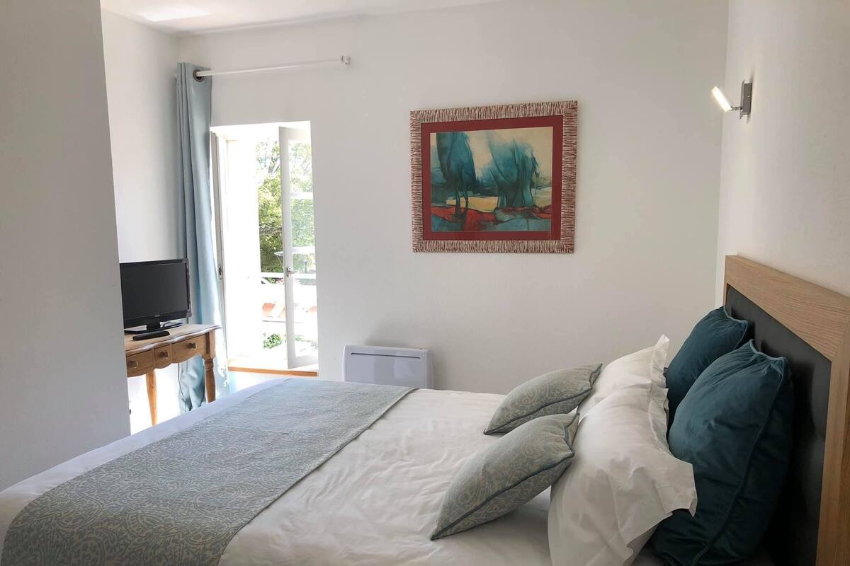 Quarto com uma cama, televisão sobre uma escrivaninha, quadro na parede e janela com cortinas.