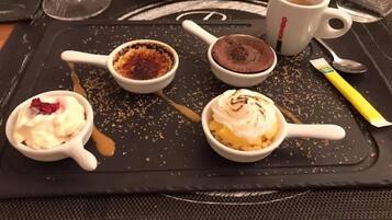 Una bandeja con cuatro recipientes de postre, una cuchara, una taza y un sobre de azúcar sobre un tapete negro.