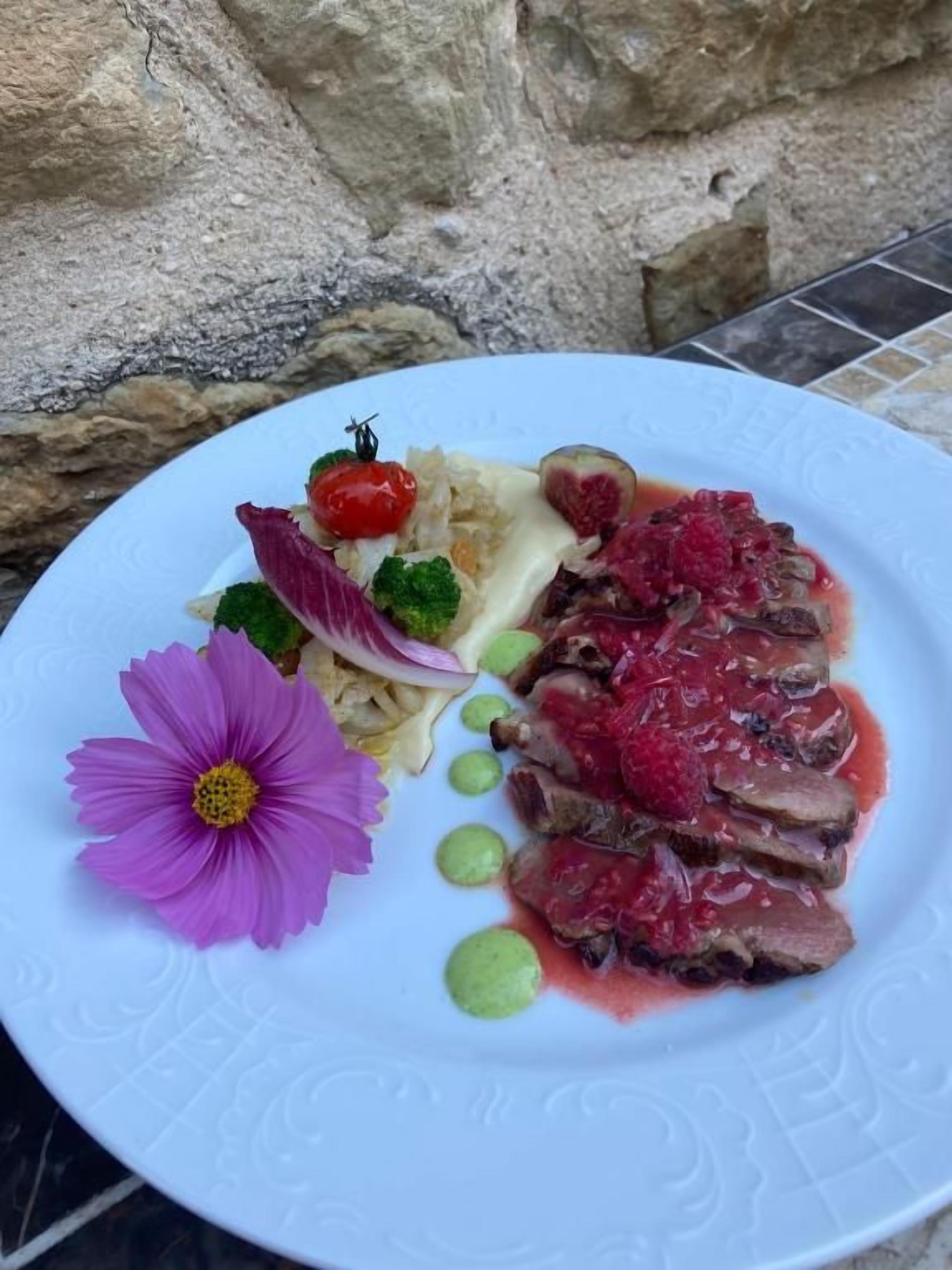 A plate of food with various items including meat, berries, and a flower.