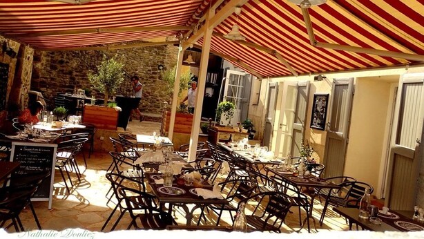 Un café al aire libre con toldos a rayas rojas y blancas, paredes de piedra y mesas preparadas para comer.