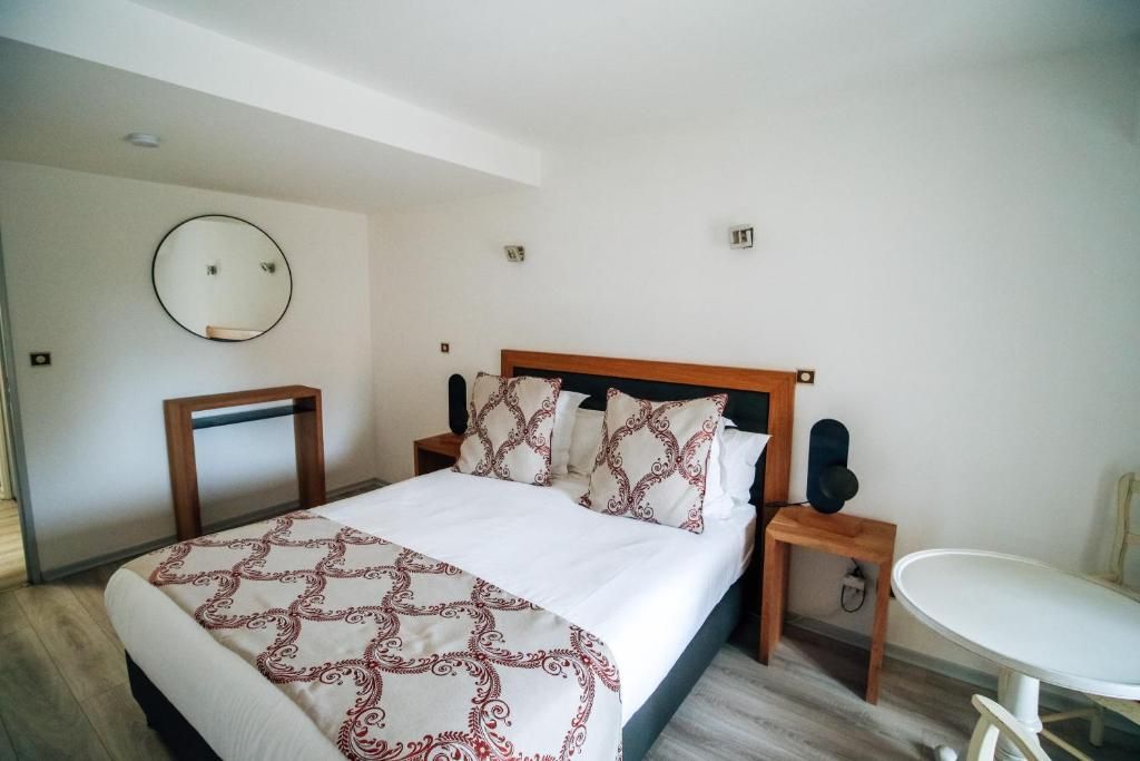 A hotel room with a bed, bedside table, chair, and a round mirror on the wall.