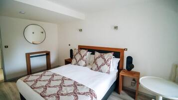 A hotel room with a bed, bedside table, chair, and a round mirror on the wall.
