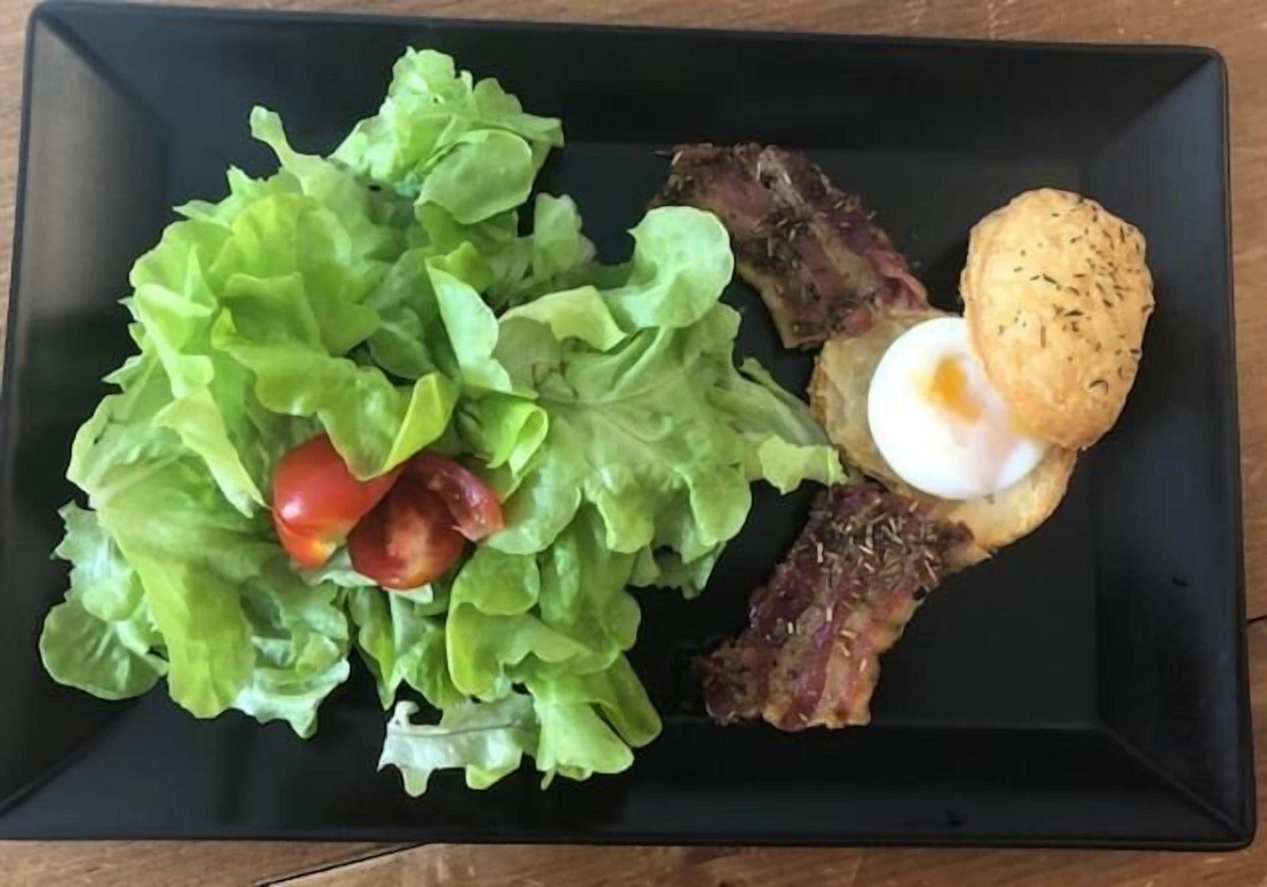 Un plato rectangular negro con ensalada, carne y un huevo frito.