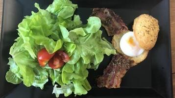 Un plato rectangular negro con ensalada, carne y un huevo frito.