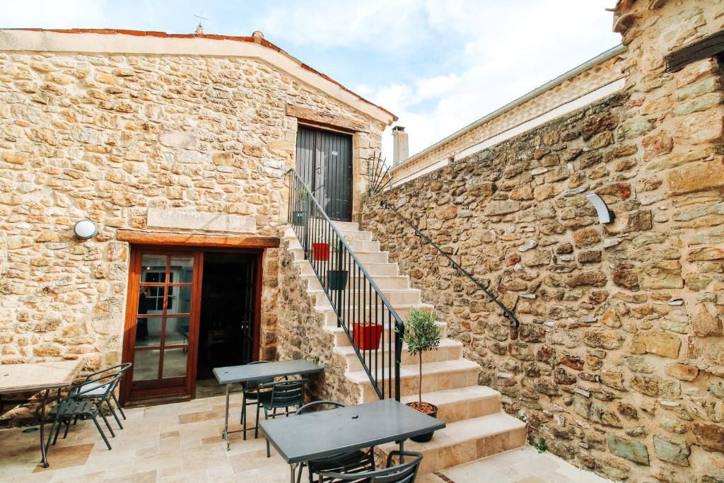 A stone building with a staircase leading to a door, outdoor seating with tables and chairs, and a small potted plant.