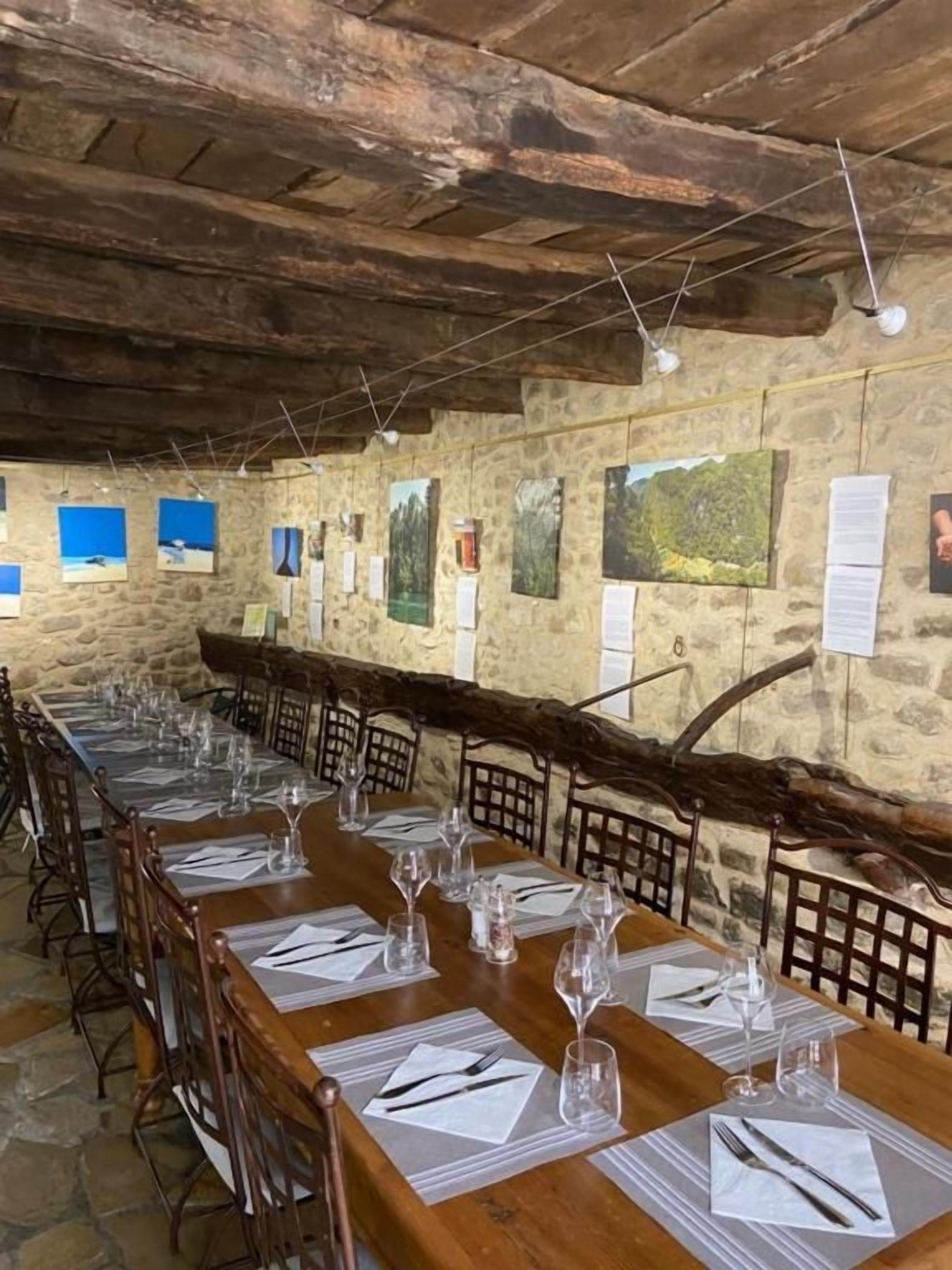 A long dining table set with chairs, wooden beams, stone walls, and artwork.