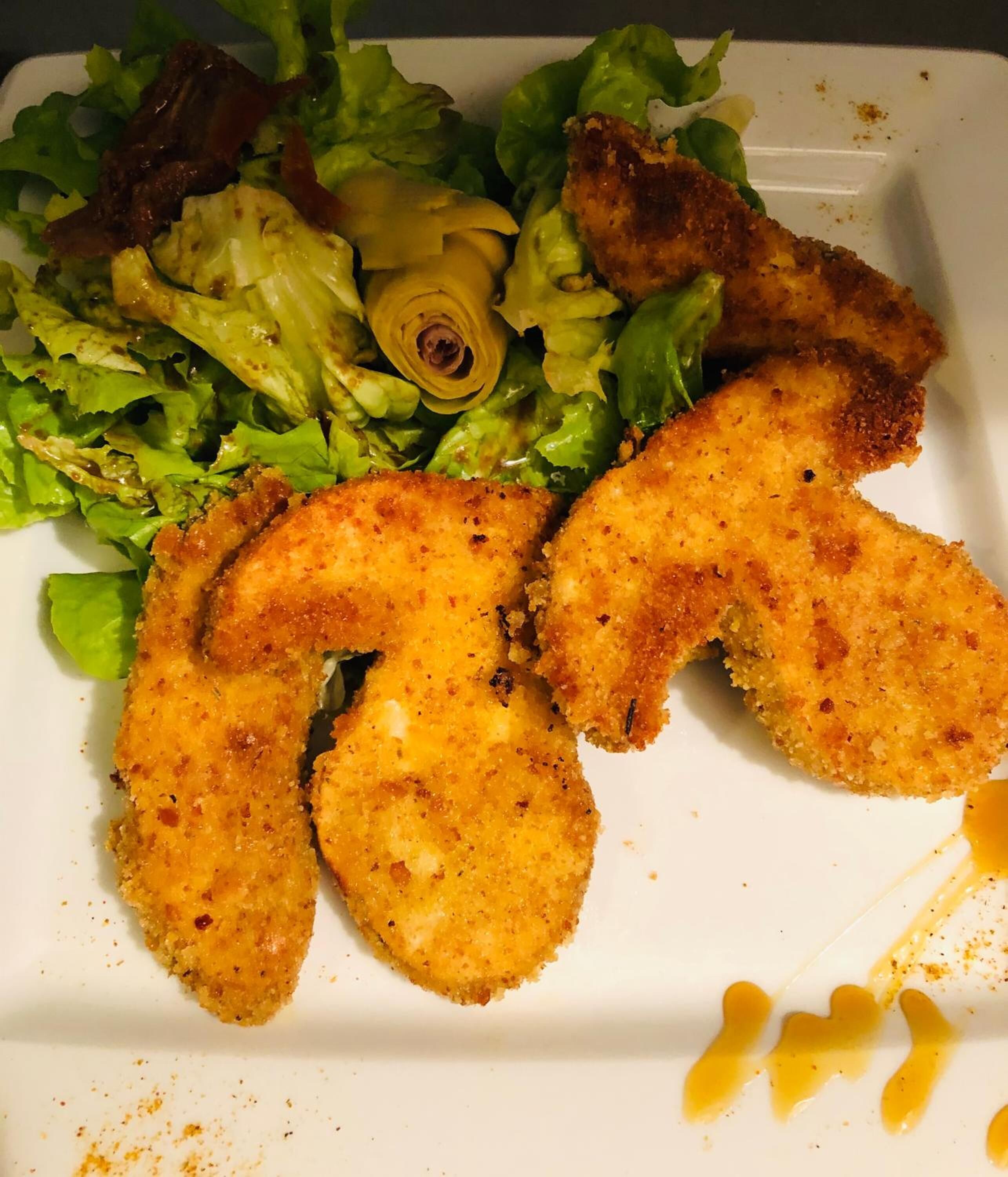 Une assiette contenant des aliments panés et frits, peut-être du poulet, accompagnée d’une salade composée de laitue et d’un légume jaune, peut-être un radis.