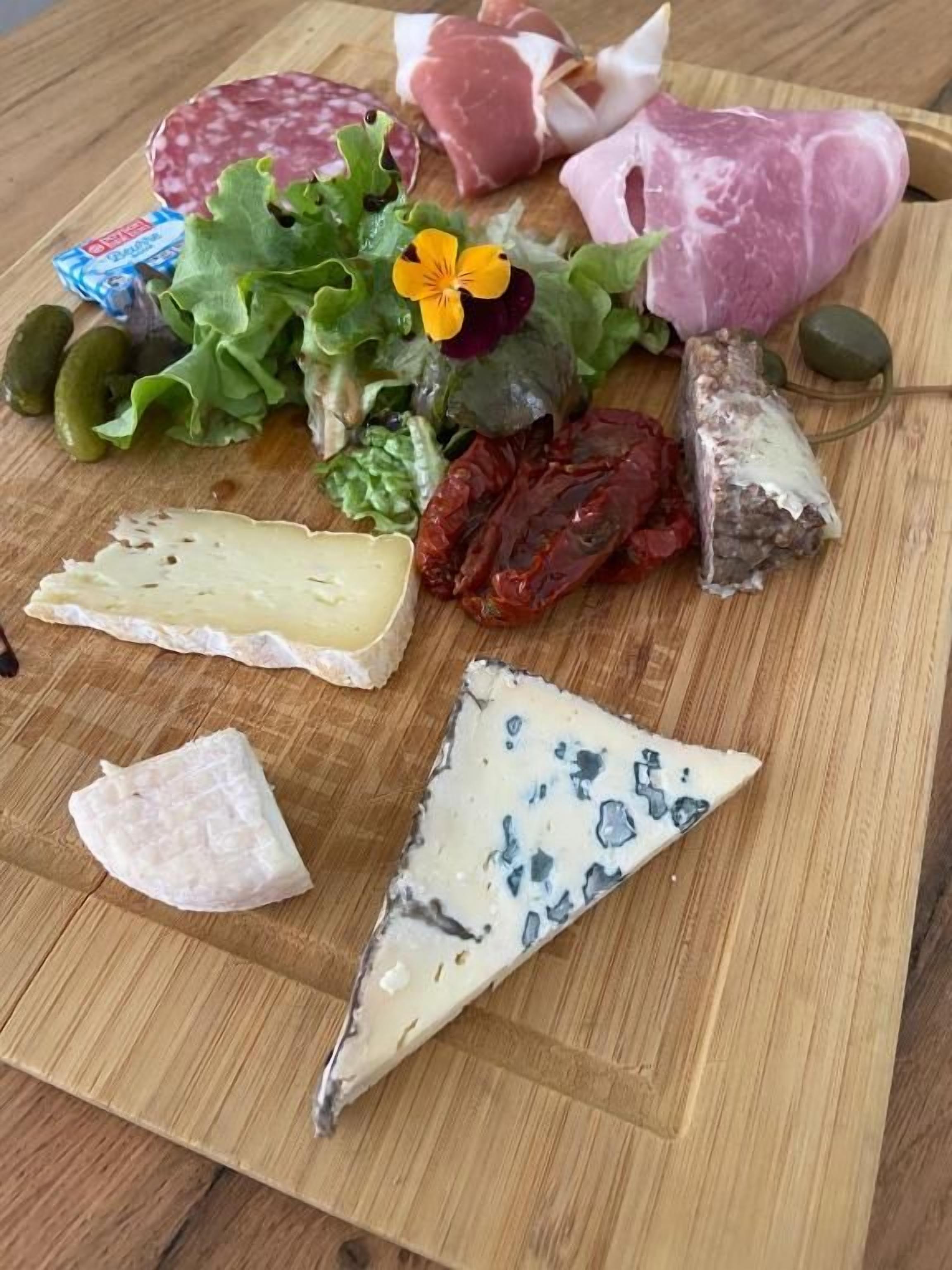 Une planche en bois garnie de différents fromages, de charcuteries et de cornichons.