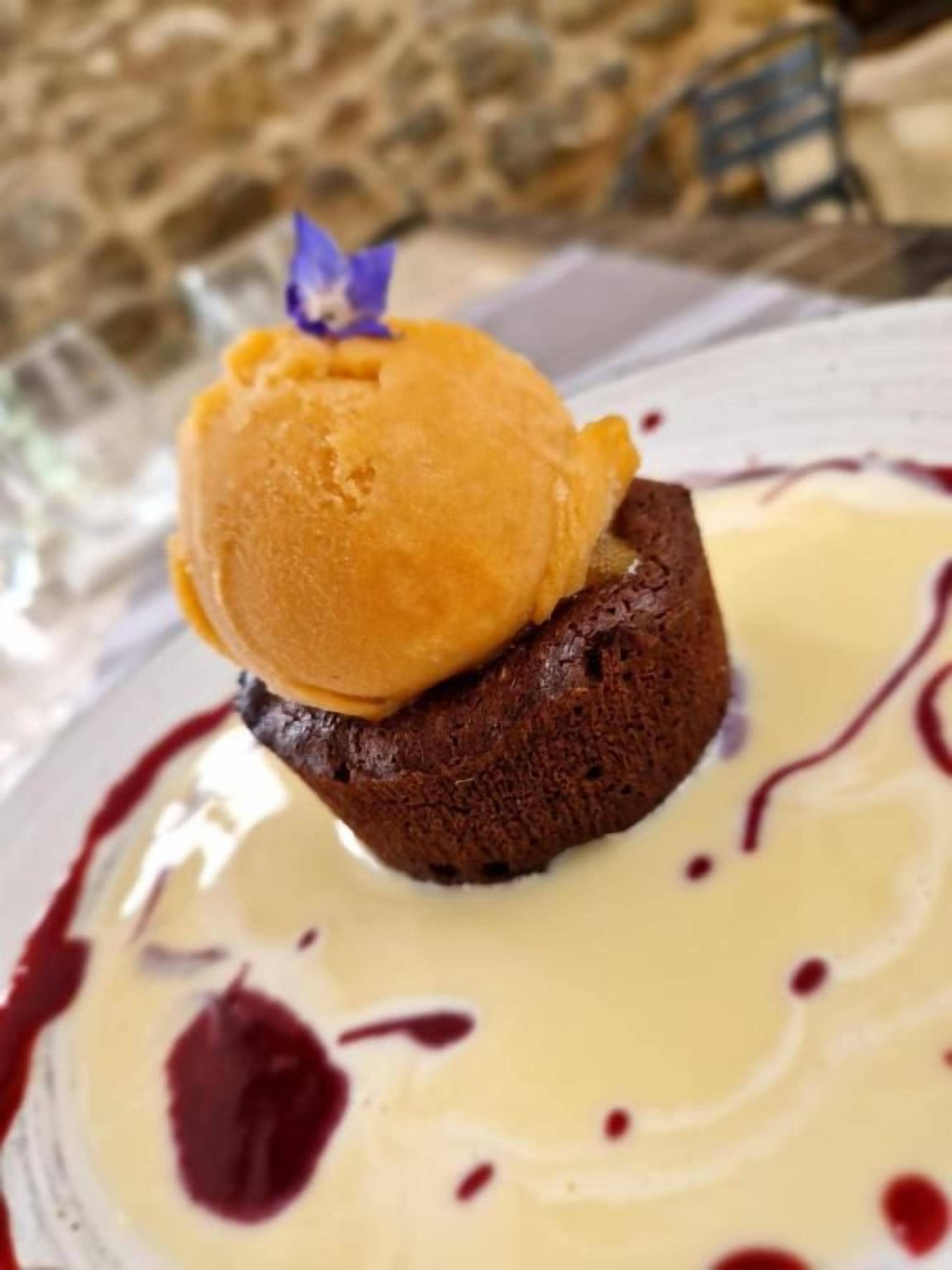 A dessert with a scoop of ice cream on top of a cake, served on a plate with a creamy sauce.