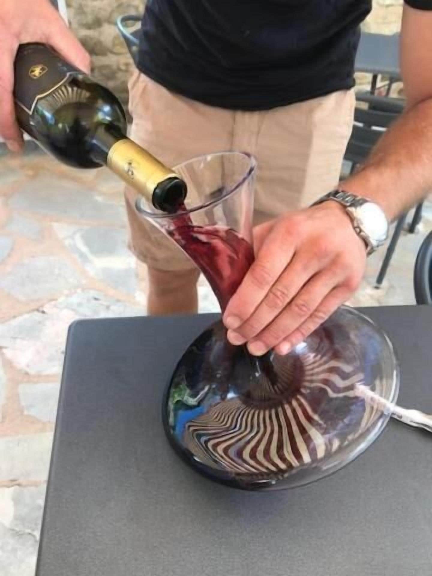 A person pouring red wine into a glass on a table.