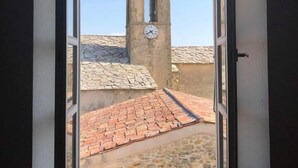 Vista a través de una ventana abierta de una torre de piedra con un reloj, cielo despejado y un camino empedrado.