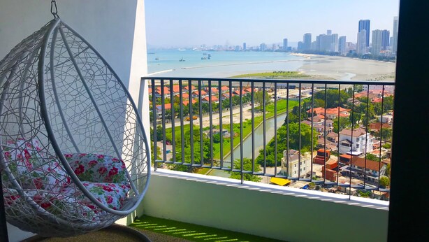 Un balcon avec un fauteuil suspendu, une vue sur une plage et un paysage urbain en arrière-plan.