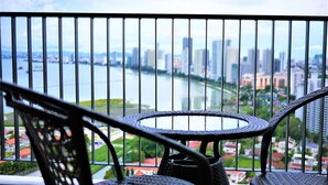 Un balcon avec des fauteuils et une table en osier, offrant une vue sur une rivière et le paysage urbain.