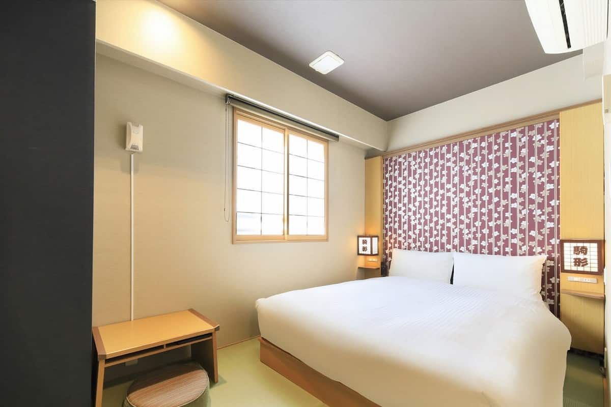 A hotel room with a bed, bedside table, lamp, and a window with a view.