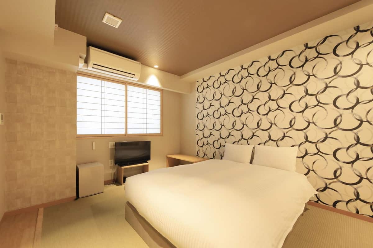 A hotel room with a bed, a TV, a window, and a patterned wall.
