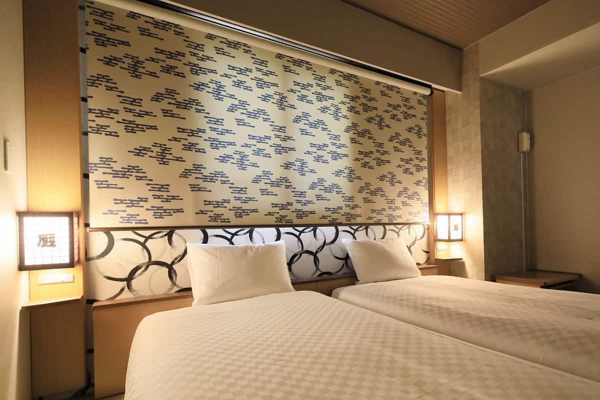A hotel room with two beds, a patterned headboard, and bedside lamps.