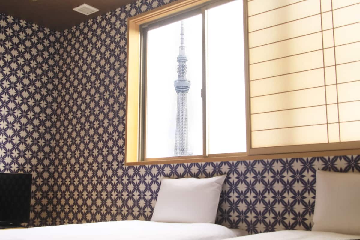A hotel room with a patterned wallpaper, a bed with white bedding, and a window with a view of a tower.