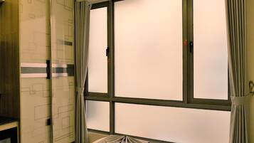 A room with a large window, curtains, and a bed with a white bedspread.
