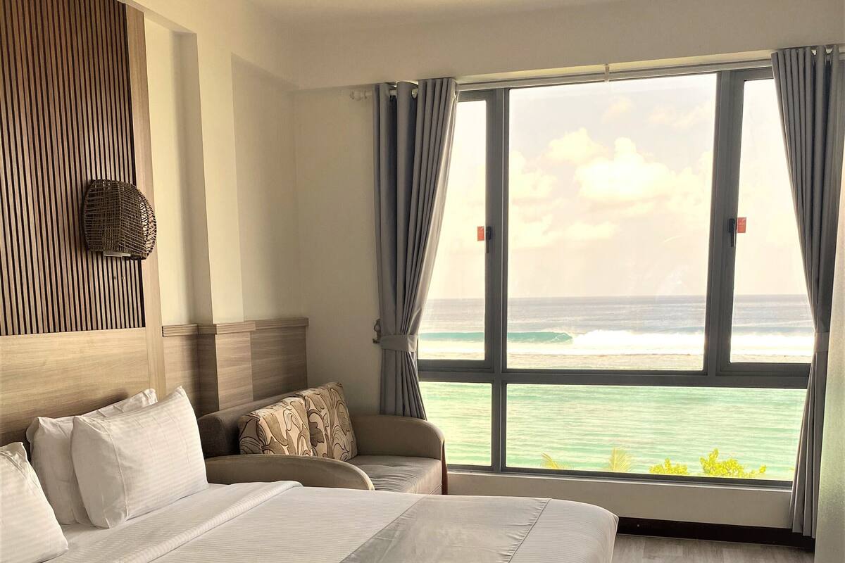 A bedroom with a large bed, a seating area, and a view of the ocean.