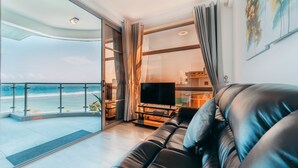 Een woonkamer met een leren bank, een flatscreen televisie en uitzicht op het strand door grote ramen.