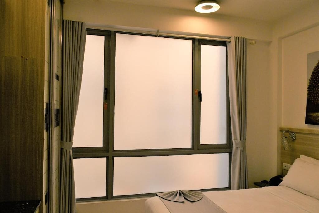 Una camera d'albergo con una grande finestra, un letto e un comodino.