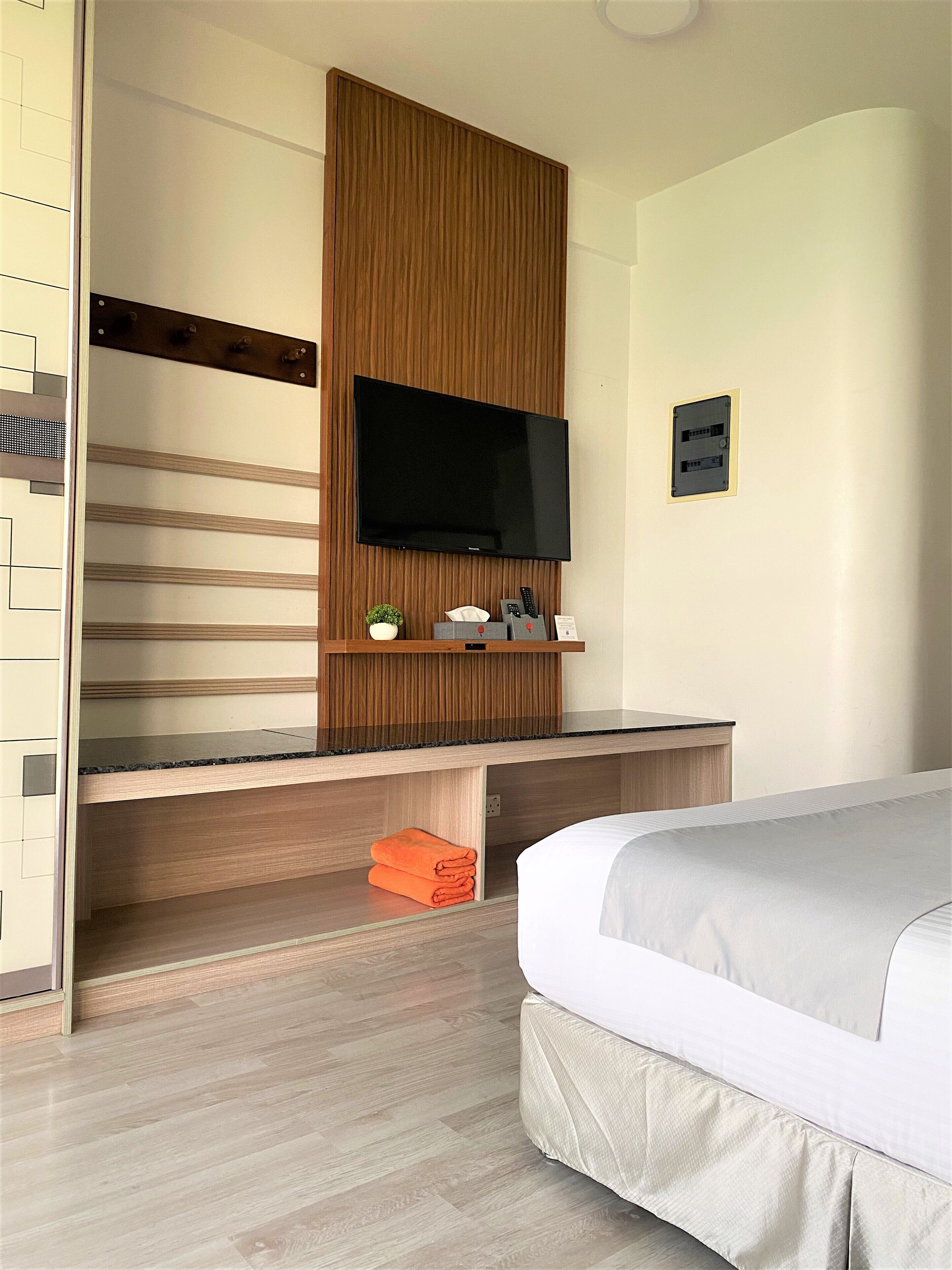 A hotel room with a flat-screen TV mounted on a wooden panel wall, a bed with white bedding, and a wooden floor.
