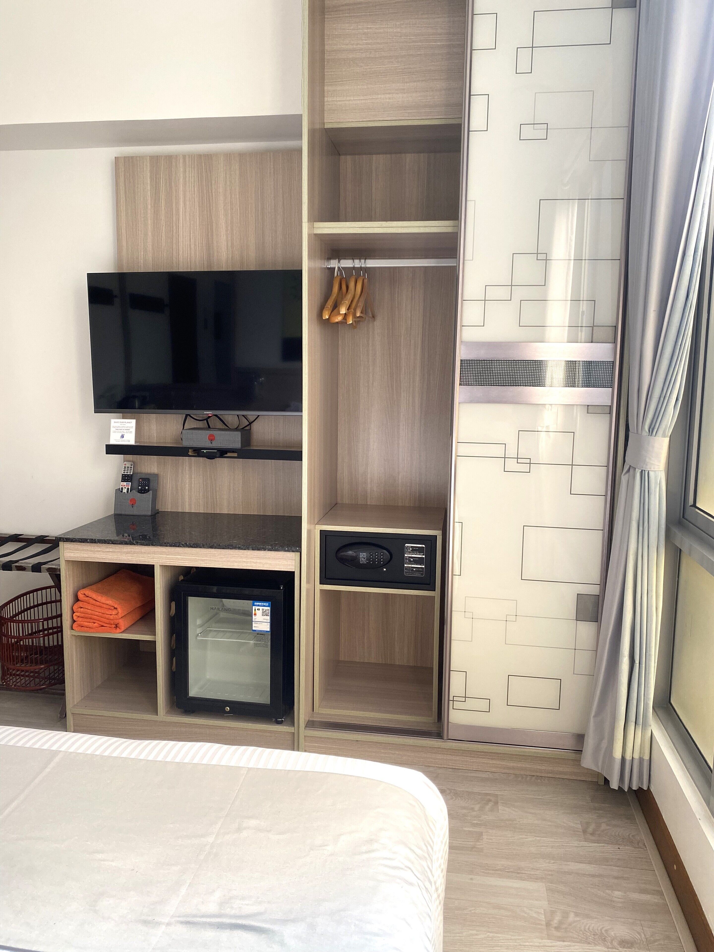 A hotel room with a bed, a TV, a minibar, a wardrobe, and a window with curtains.