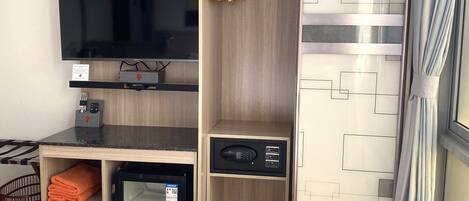 A hotel room with a bed, a TV, a minibar, a wardrobe, and a window with curtains.