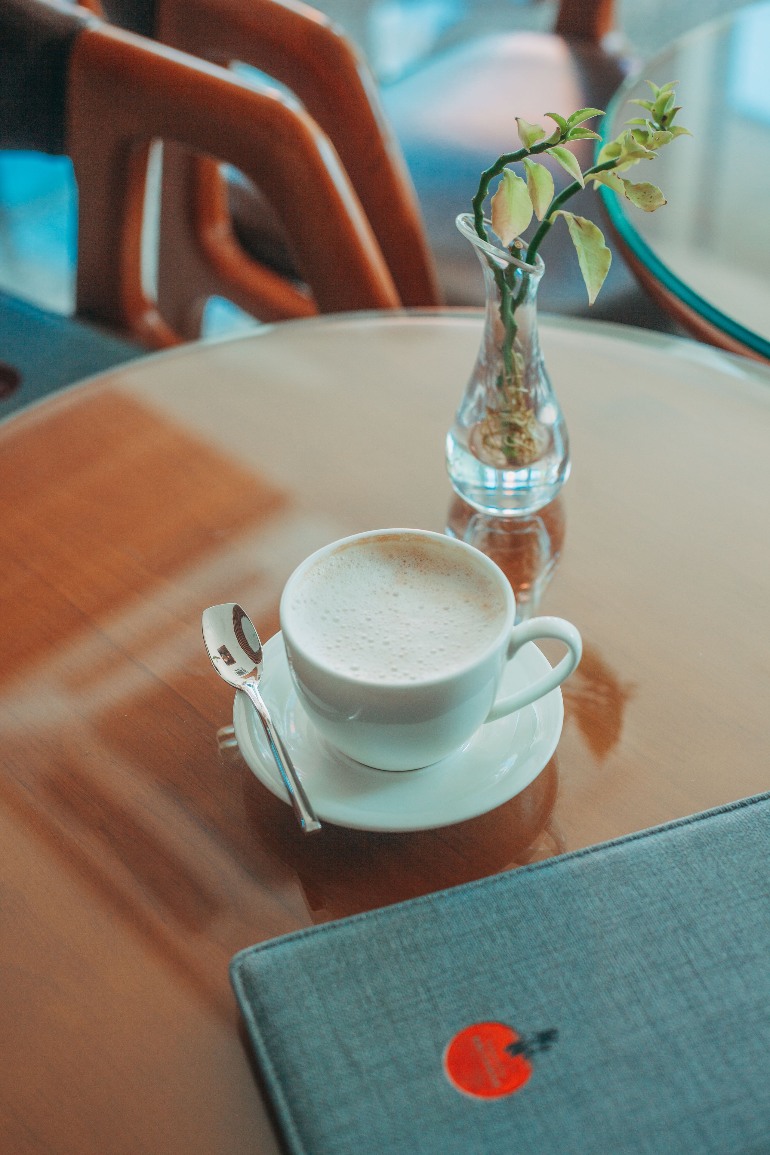 Una taza de café sobre un plato, un pequeño florero con una planta y una computadora portátil sobre una mesa de madera.