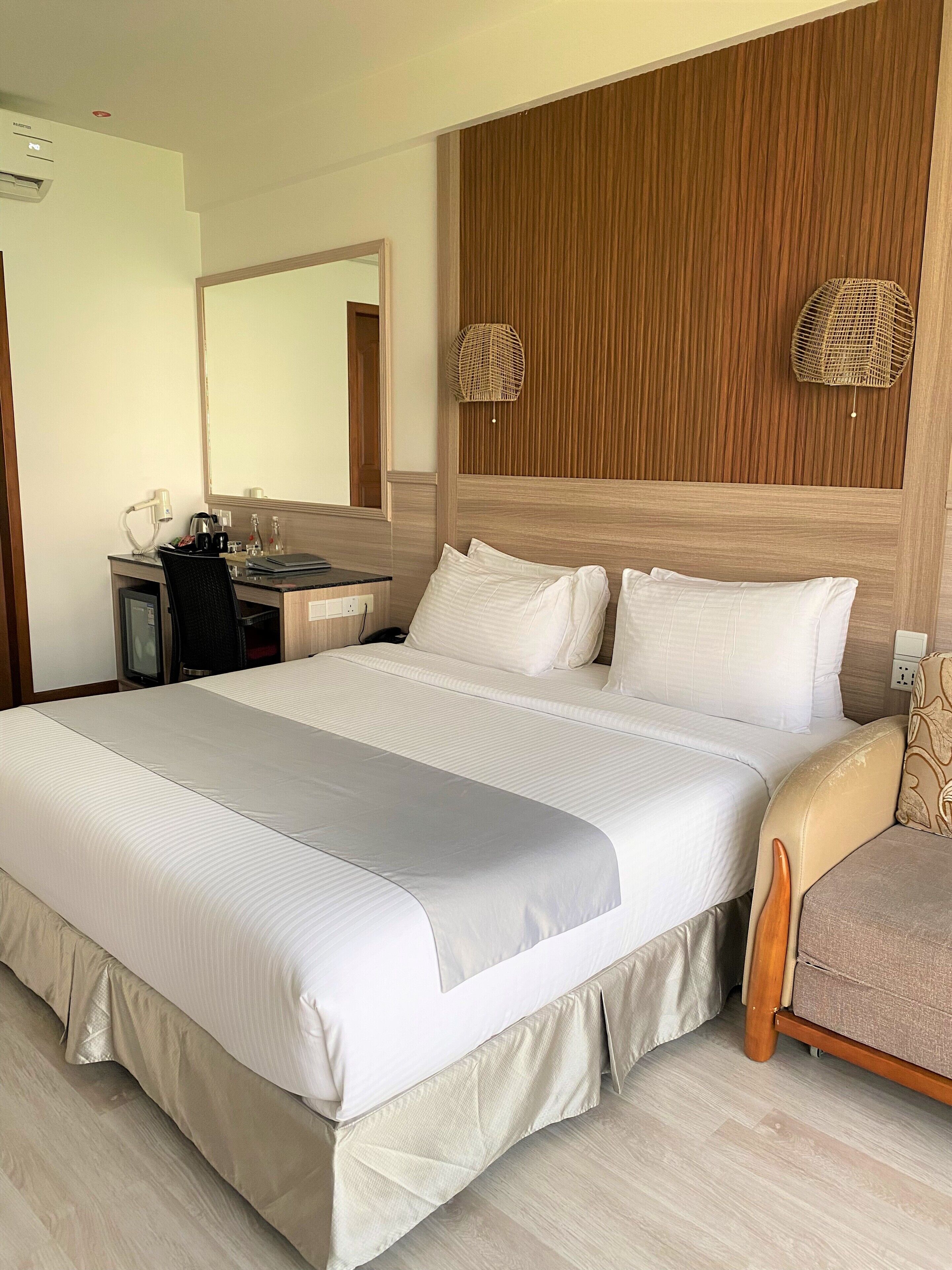 A hotel room with a large bed, a desk with a chair, a mirror, and a wooden headboard.