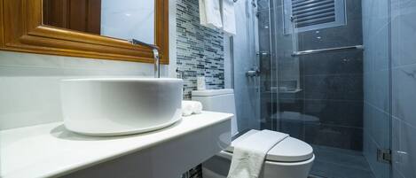 Un baño moderno con un lavamanos grande de color blanco, un inodoro y una ducha con mampara de vidrio.