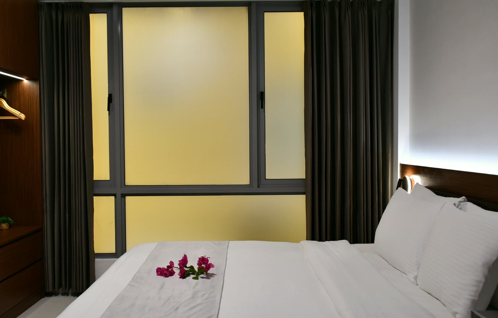 A hotel room with a bed, a nightstand, a lamp, and a window with curtains.