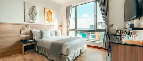 A hotel room with a large bed, a desk with a flat-screen TV, and a balcony with a view of the city.
