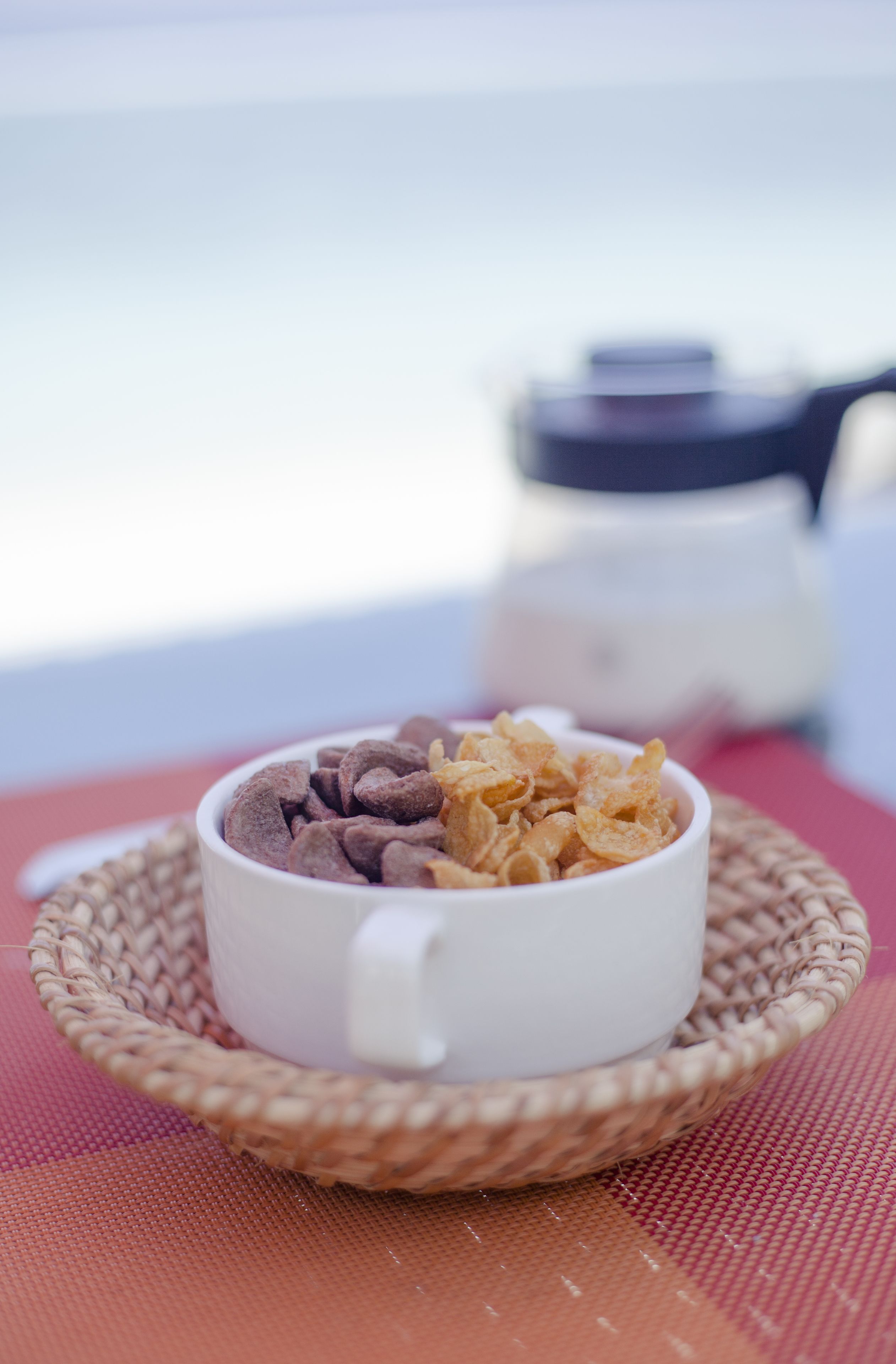 A white cup filled with chocolate and cereal flakes on a woven placemat.
