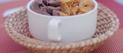 A white cup filled with chocolate and cereal flakes on a woven placemat.