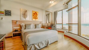 Een moderne hotelkamer met een groot bed, een bureau en uitzicht op het strand.