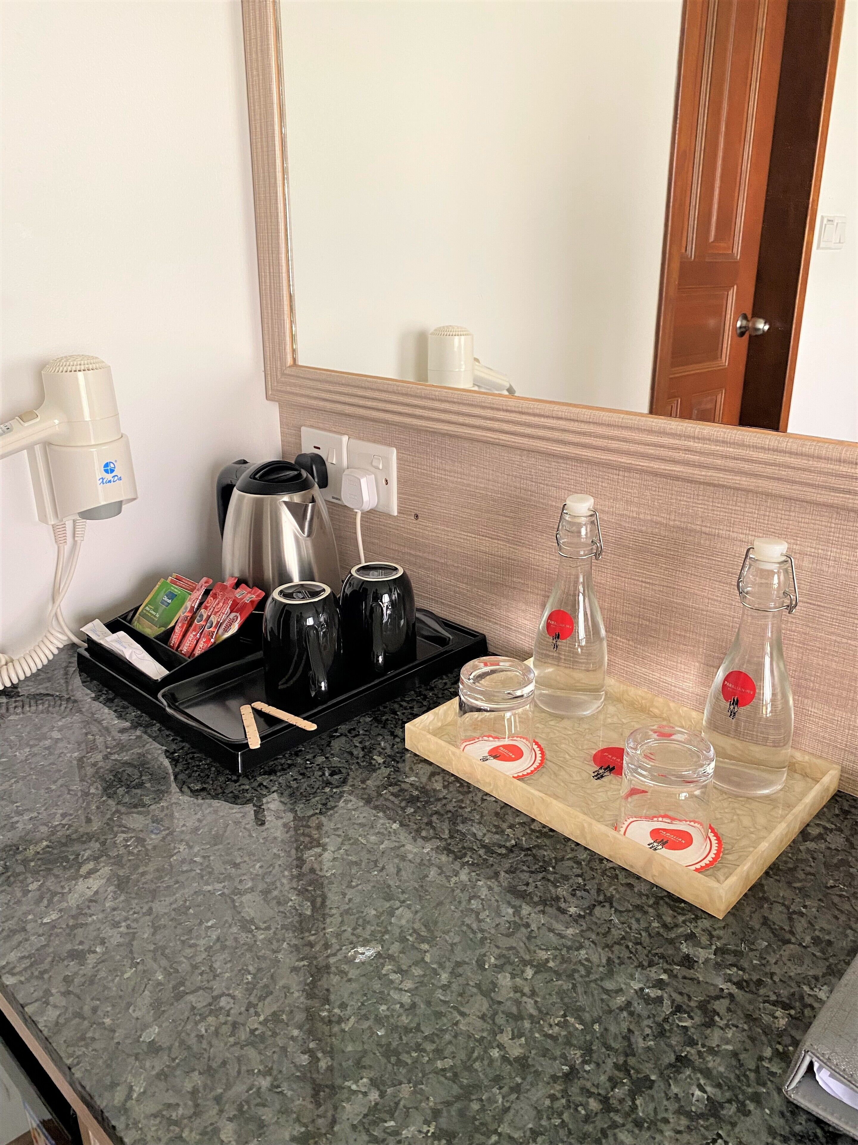 A hotel room with a granite countertop, a hairdryer, a coffee maker, and two bottles of water.