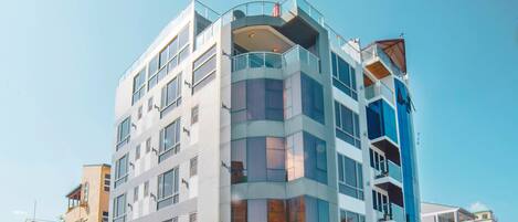 A multi-story hotel with a modern design, featuring balconies, large windows, and a ground-level restaurant.