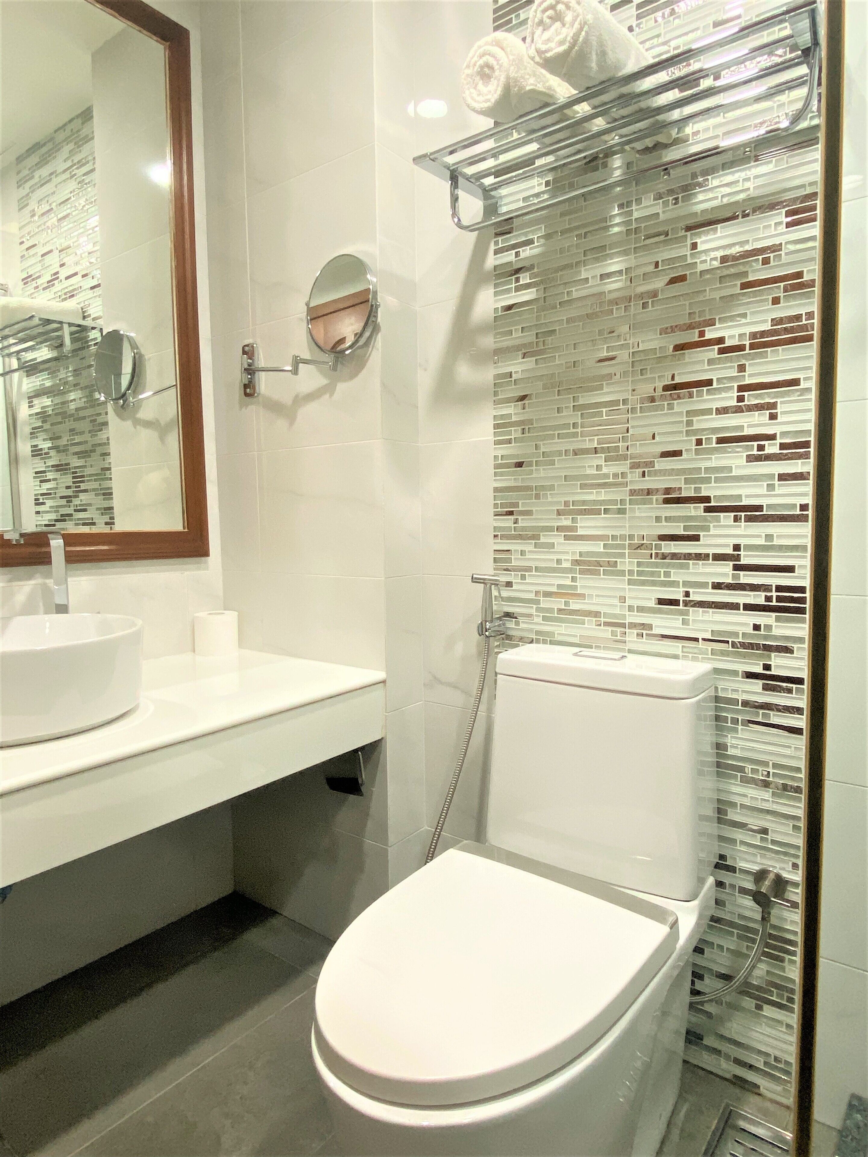 Un bagno moderno con il water bianco, uno specchio rotondo e una cabina doccia in vetro.