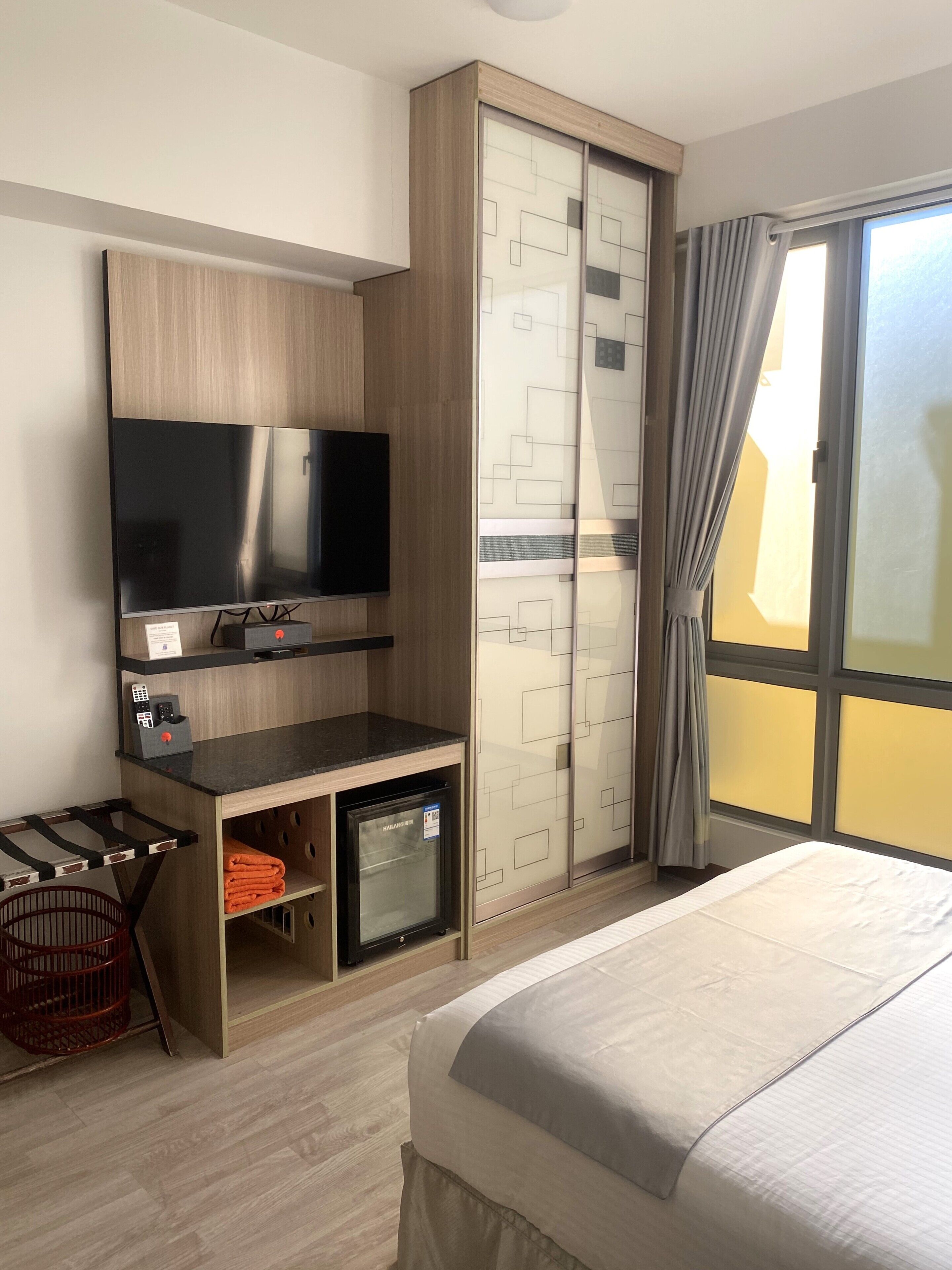 A hotel room with a bed, a desk with a flat-screen TV, a minibar, and a sliding door closet.