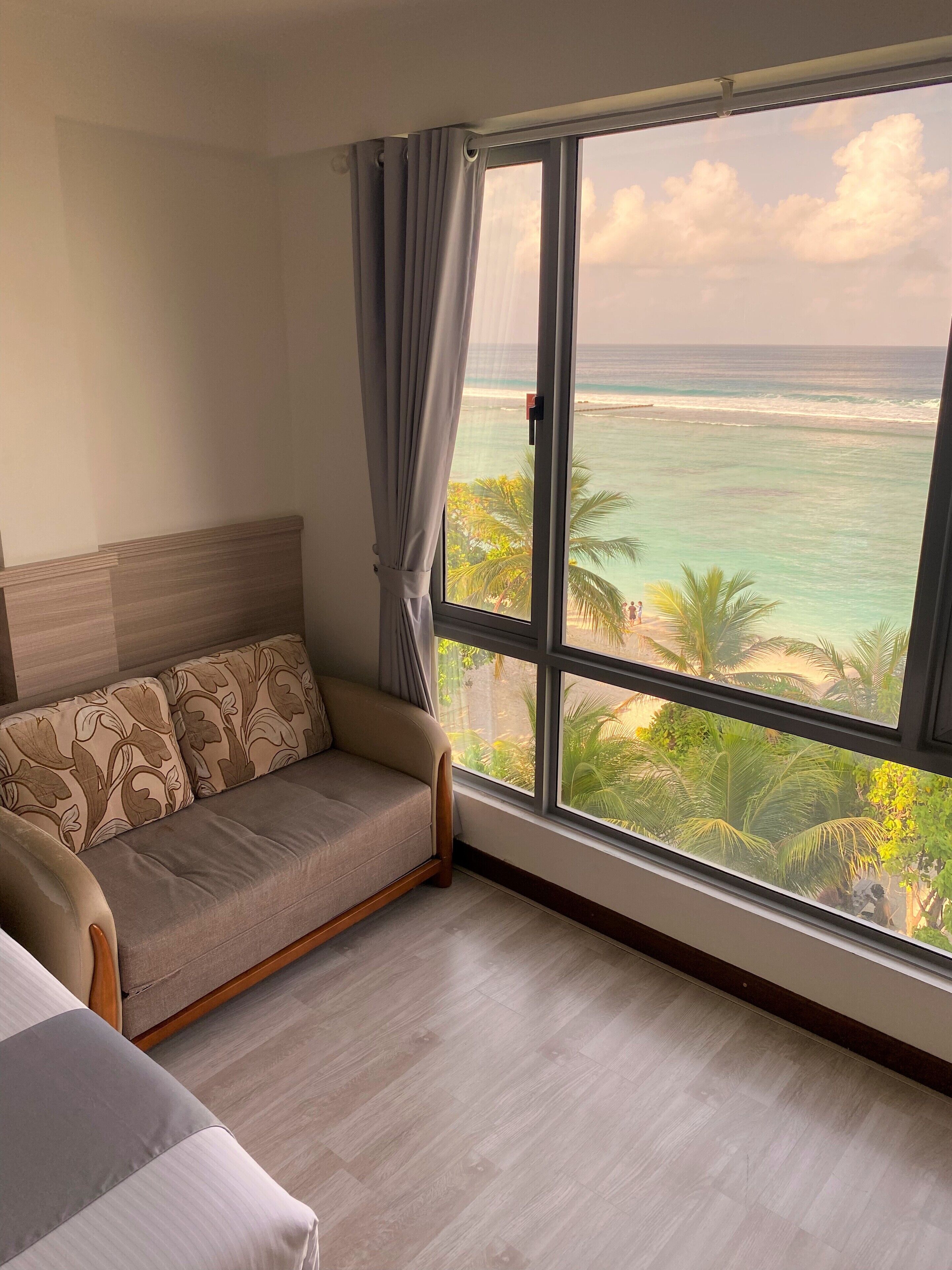 A room with a large window offering a view of the ocean and palm trees.