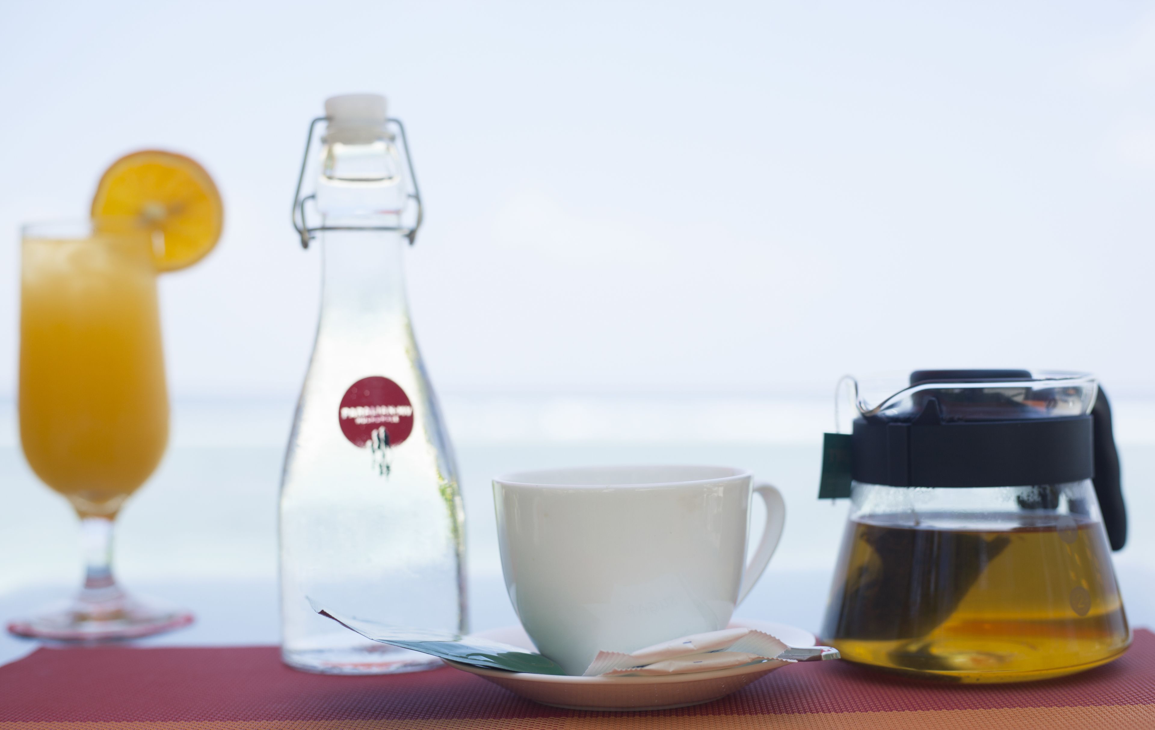 A table with a glass of orange juice, a bottle of water, a white cup, and a coffee maker.