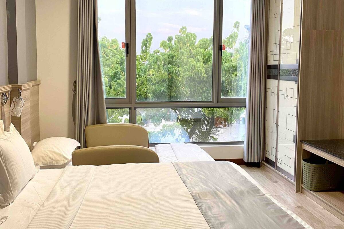 A hotel room with a large bed, a chair, a desk, and a view of greenery outside.