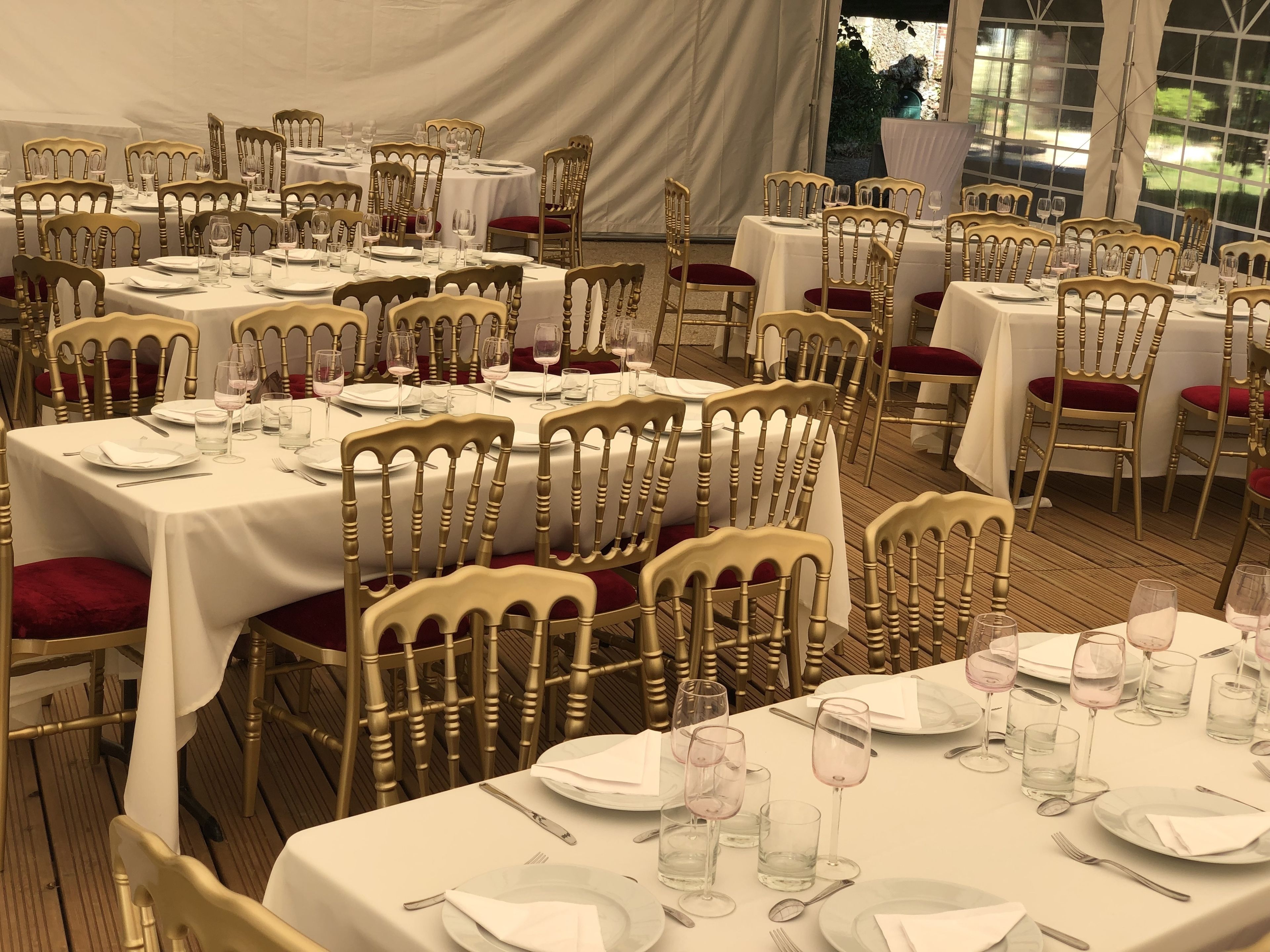 Un salón de banquetes con mesas redondas, sillas doradas y manteles blancos.